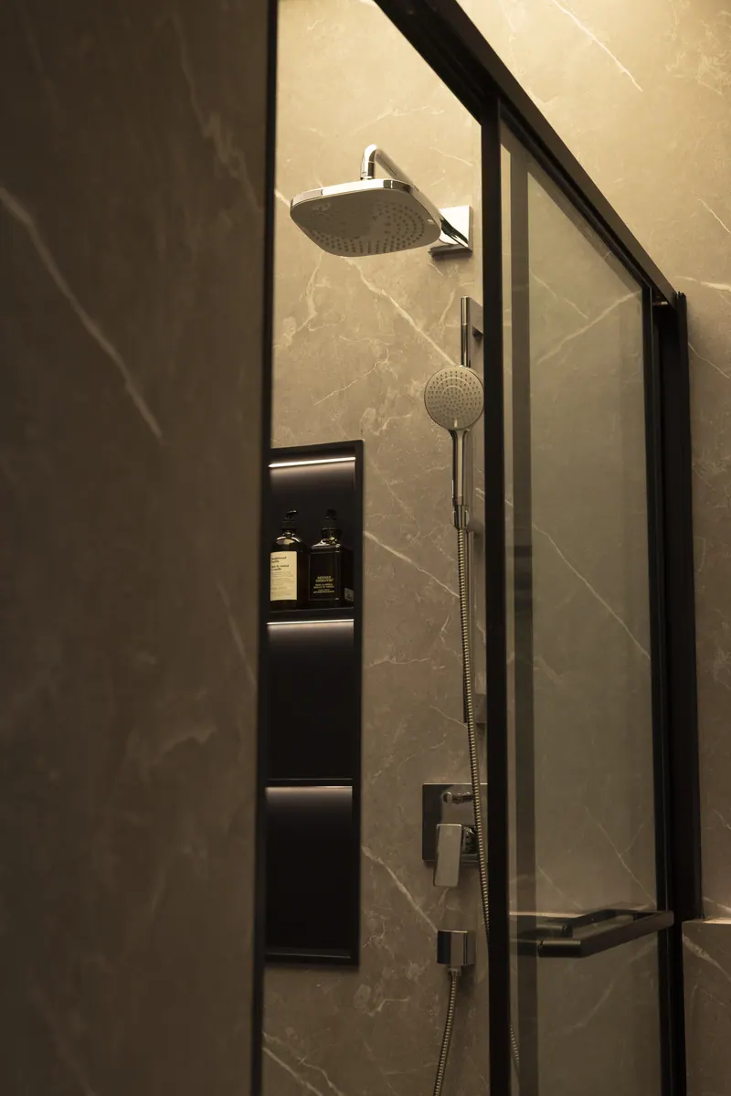 Stone-look shower with a rain head behind black-framed glass
