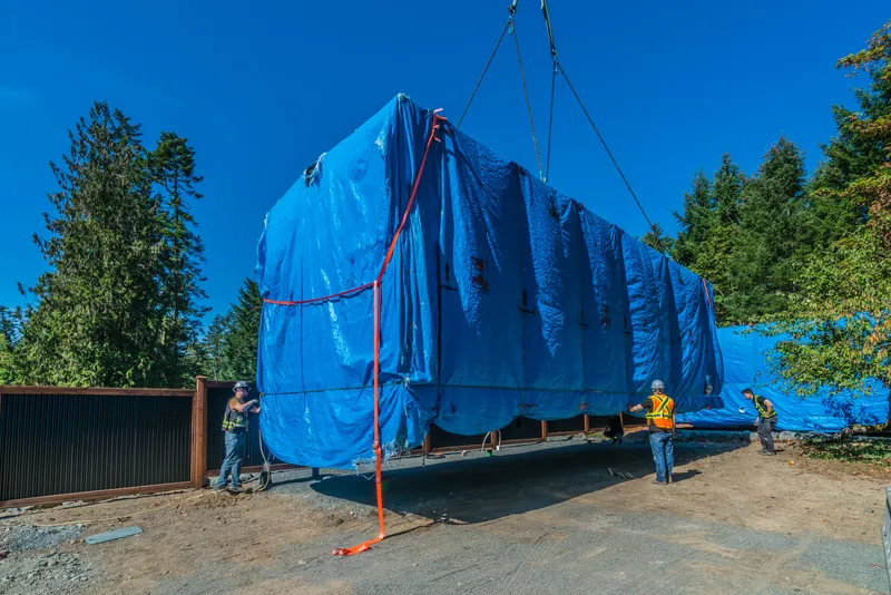 A Cueva home under a blue weather tarp being lowered by crane while the crew guides it into place