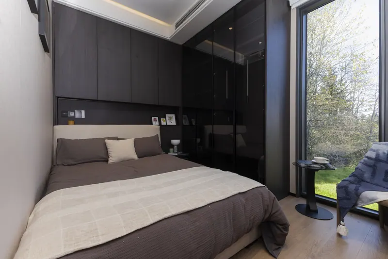 Dark-finish main bedroom with the wardrobe wall, headboard shelf and a reading chair by the window