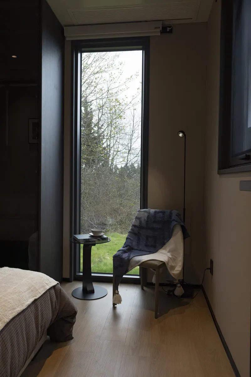 Reading corner with an armchair, side table and a tall window onto trees