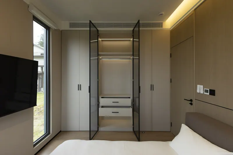 Light-finish bedroom with the wardrobe open, a wall TV and a window