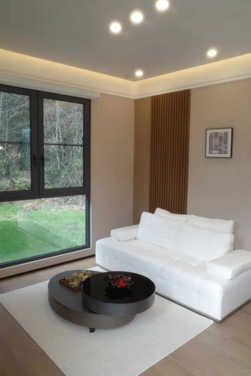 Light-finish living room with a white sofa, oak slat wall and a large window onto the lawn