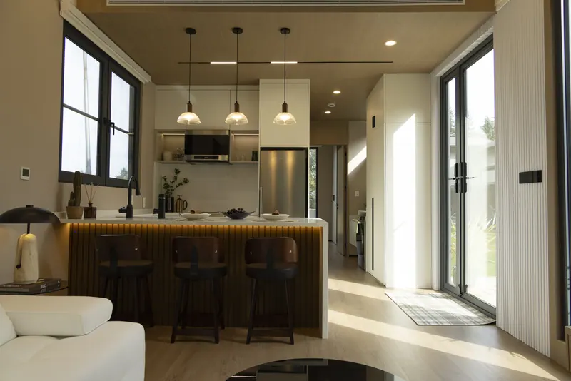 Sunlit show-home kitchen with a quartz waterfall island, pendant lights and glass doors