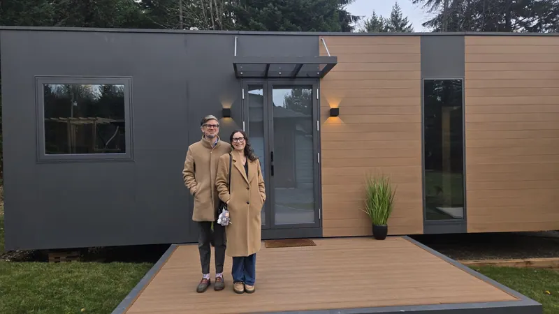 A couple at the entrance of a show home at dusk, with the wall lights on