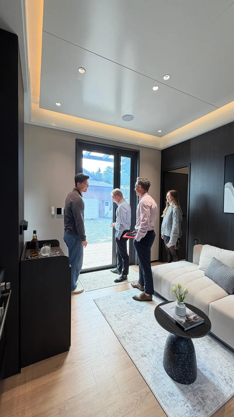 Visitors smiling by the tall glass door in the dark-finish living room